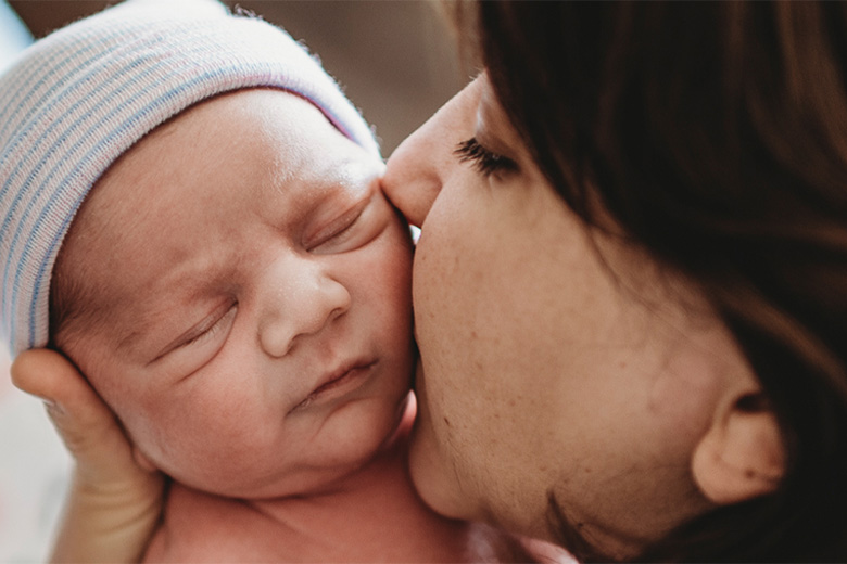Mother kisses newborn baby's cheek